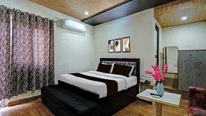 A bedroom with a bed, bedside table, bench, and a small table with a vase. - Deluxe Hotel Shhalom (Haldwani)