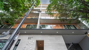 Un bâtiment moderne doté d’une façade en béton, d’une entrée bien visible et d’un balcon avec des garde-corps en verre.