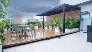 Une terrasse sur le toit dotée d’une plateforme en bois, de chaises vertes, d’une table, de plantes en pot et d’une structure en forme de pergola.