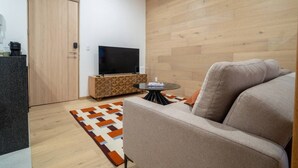 Un salon moderne avec un canapé, un téléviseur posé sur un meuble en bois, une petite table ronde et un tapis à motifs.