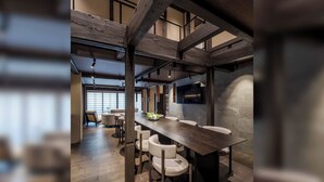 Un intérieur moderne avec des poutres apparentes, une longue table à manger entourée de chaises et un téléviseur à écran plat fixé au mur.