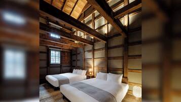 Una habitación con vigas de madera, una cama grande, una cama más pequeña, un ventanal y una lámpara.