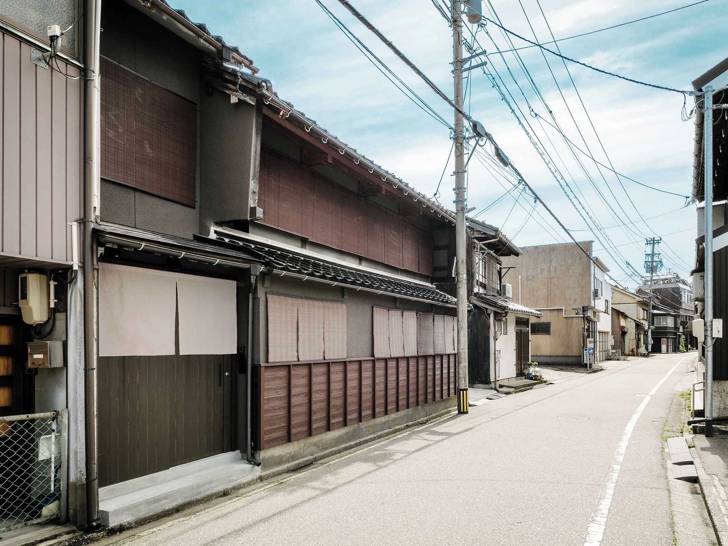 A narrow urban street with traditional buildings, a utility pole, and overhead power lines.