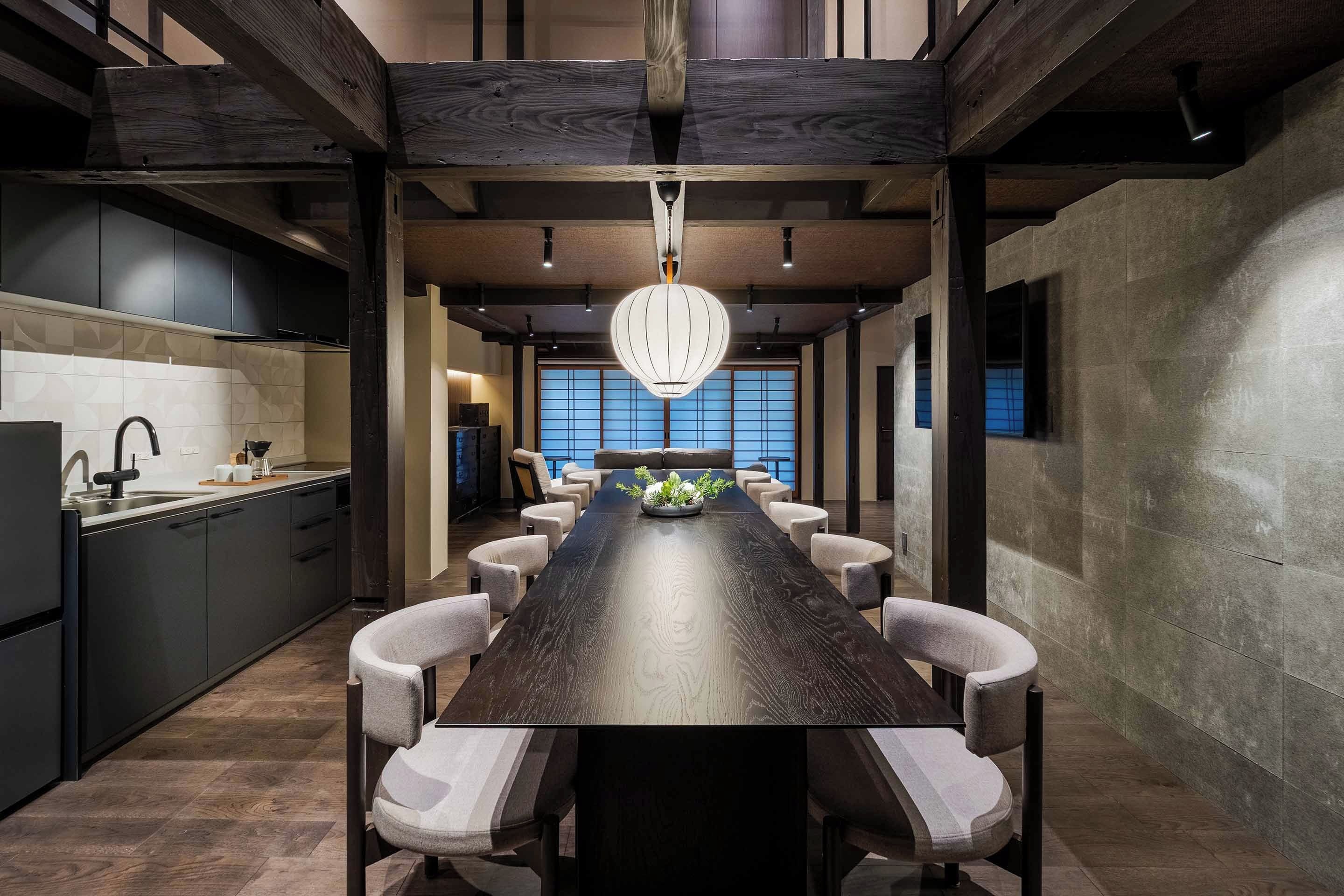 A modern kitchen with dark cabinetry, a central island, and a dining area with a long table and chairs.