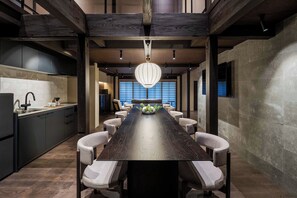 Une cuisine moderne avec des meubles de couleur sombre, un îlot central et un coin repas comprenant une longue table et des chaises.