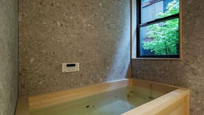 Une baignoire avec un panneau de commande intégré dans un mur texturé, une fenêtre donnant sur un paysage verdoyant et un cadre en bois.