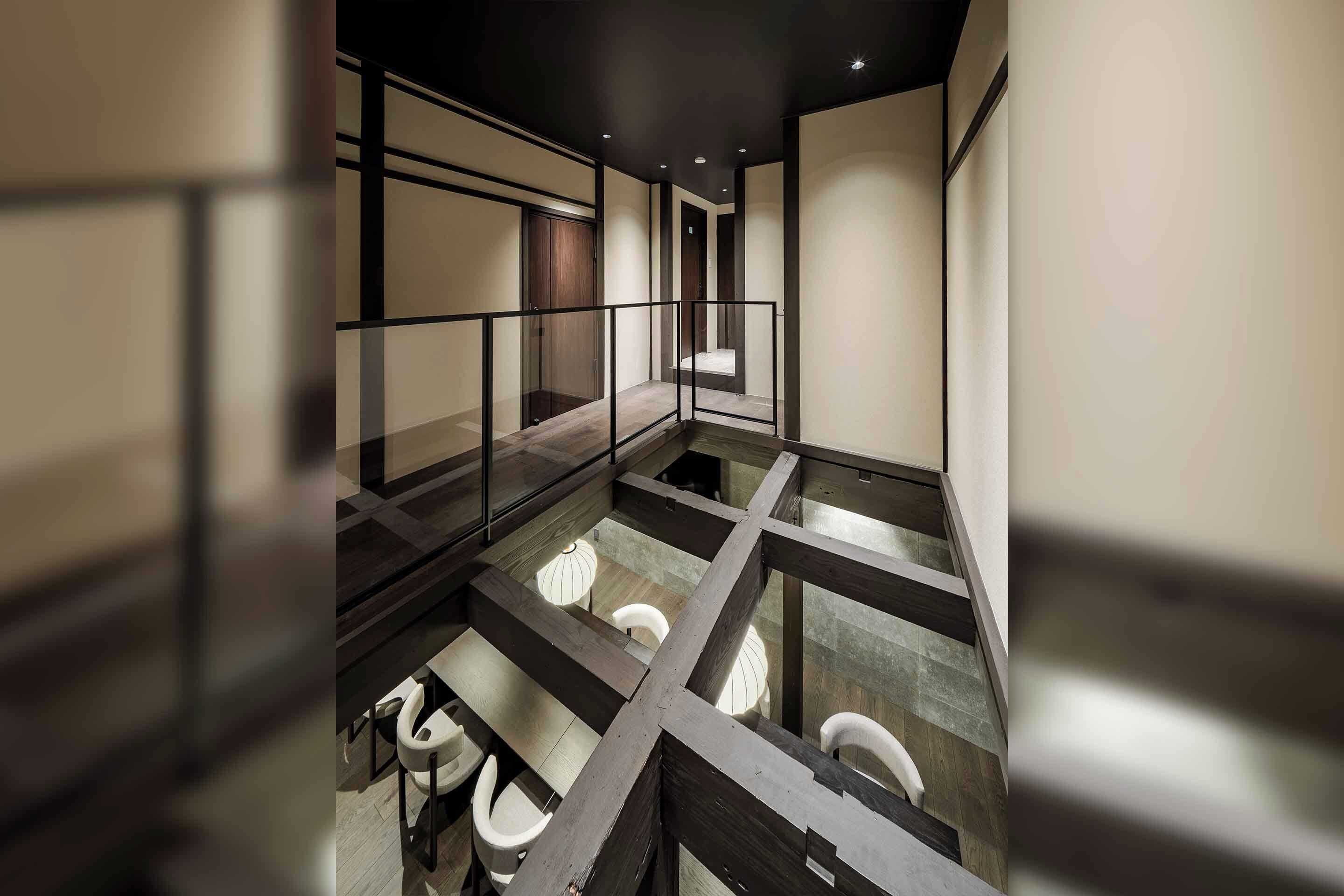 A modern interior with a glass railing, a wooden floor, and a seating area with chairs.