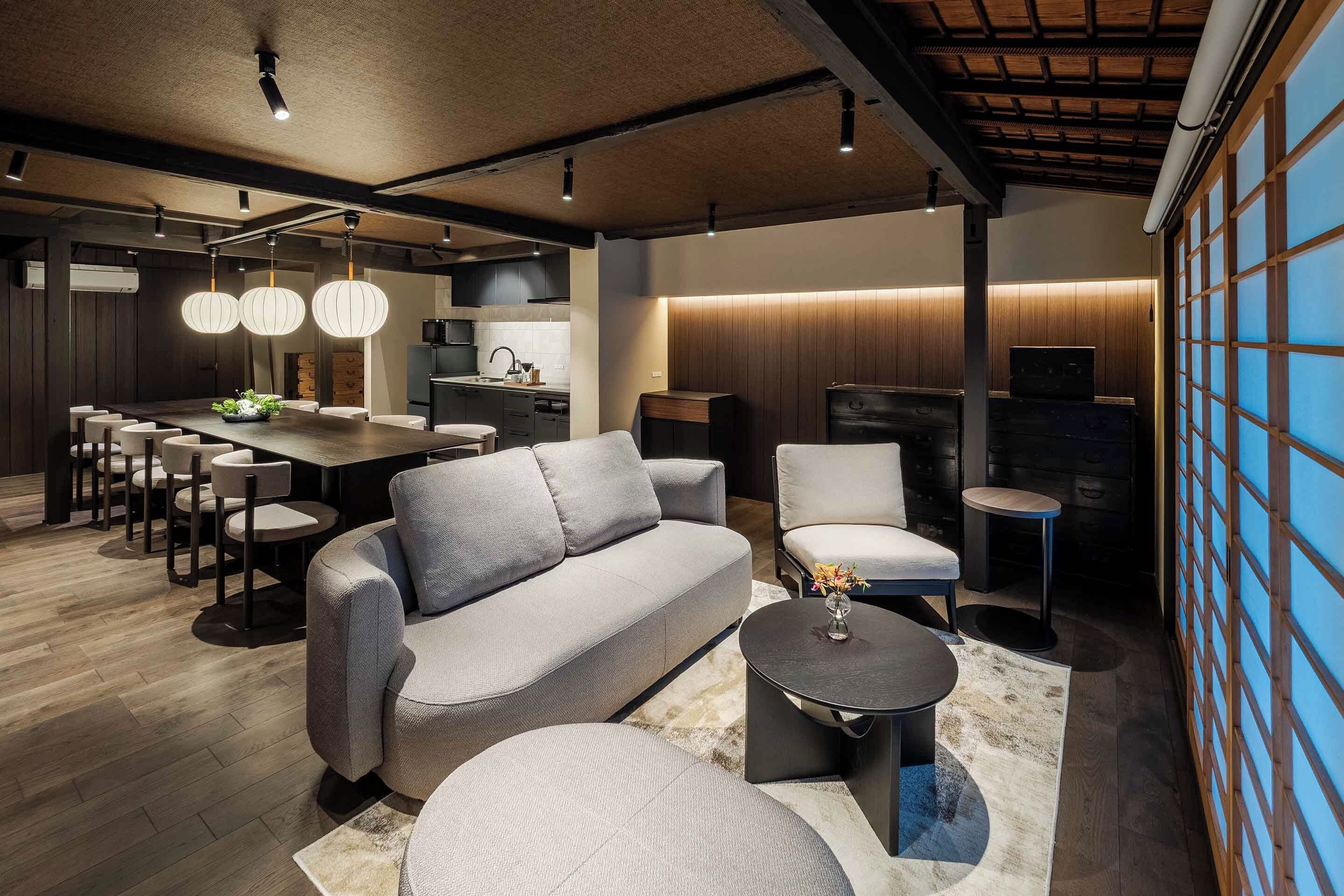 A modern living room with a grey sofa, a round coffee table, and a dining area with a kitchen in the background.