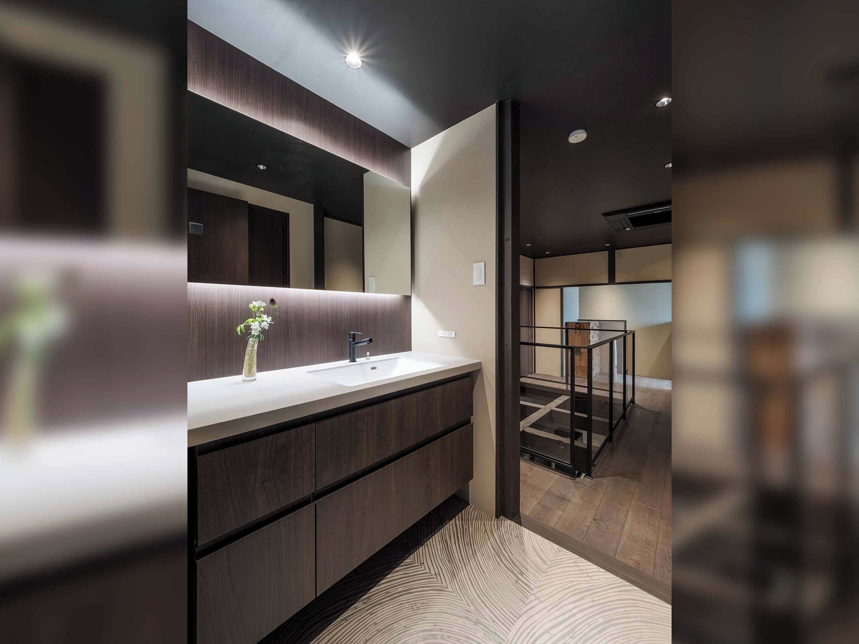 A modern bathroom with a large mirror, dark wood cabinetry, and a white countertop.