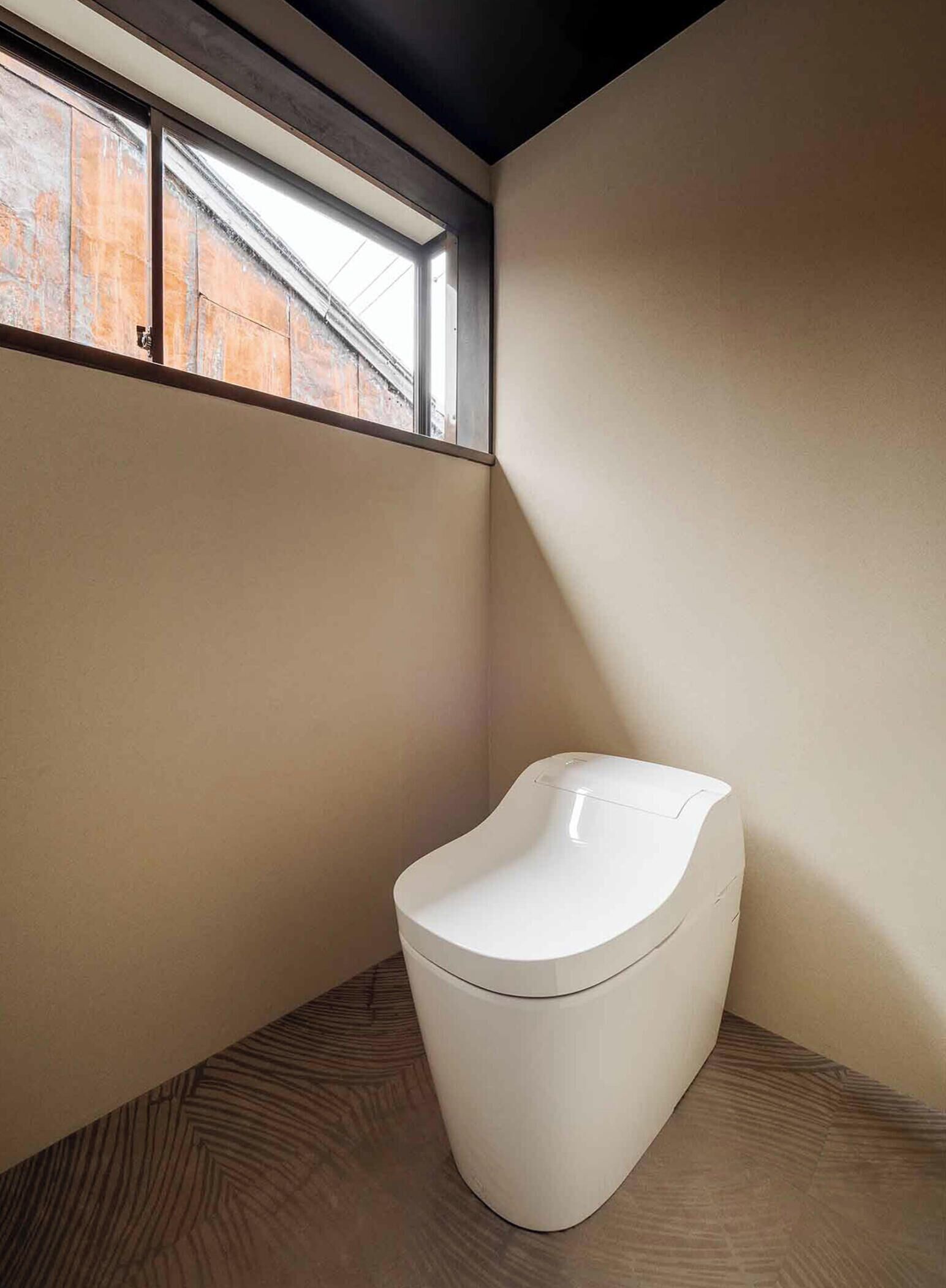 Des toilettes modernes, installées dans un coin d’une pièce, avec une fenêtre au-dessus.