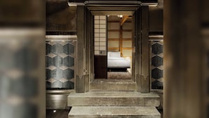 Una habitación japonesa tradicional con suelo de tatami, una cama de madera baja y una puerta corredera que da a otra estancia.