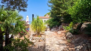 A stone pathway leading to a building with a tiled roof, surrounded by lush greenery and a clear blue sky. - Casa Horizont - Denia, Costa Blanca (Denia)