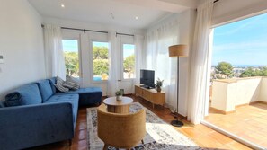 Ein modernes Wohnzimmer mit einem blauen Sofa, einem Fernseher, einem kleinen runden Tisch und einem Balkon mit Blick.
