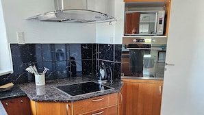Une cuisine moderne avec un pare-feu en marbre noir, des armoires en bois, une hotte de cuisinière en acier inoxydable et un four encastré.