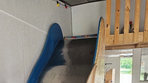 Un toboggan en bois dans une pièce dont le sol est en béton et les murs sont blancs.