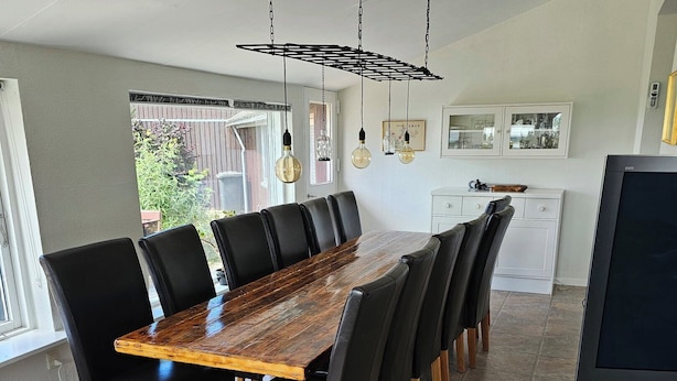 Un espace repas avec une longue table en bois, des chaises noires et des luminaires suspendus.