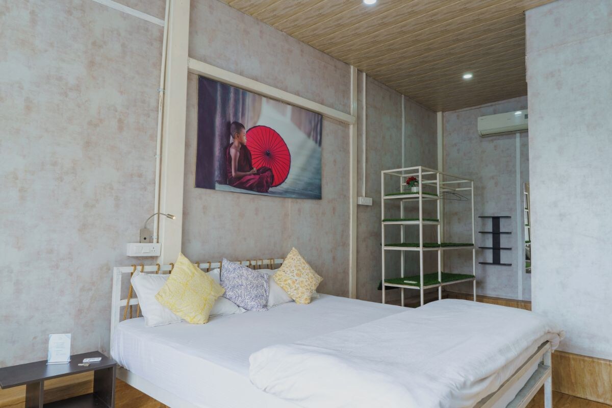 Habitación de hotel con cama, mesita de noche, estante en la pared y un cuadro.