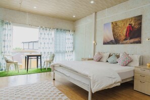 Un dormitorio con cama, mesitas de noche, una silla y una ventana con cortinas.