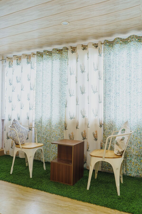 Una habitación con dos sillas blancas, una pequeña mesa de madera y un suelo de césped artificial verde.