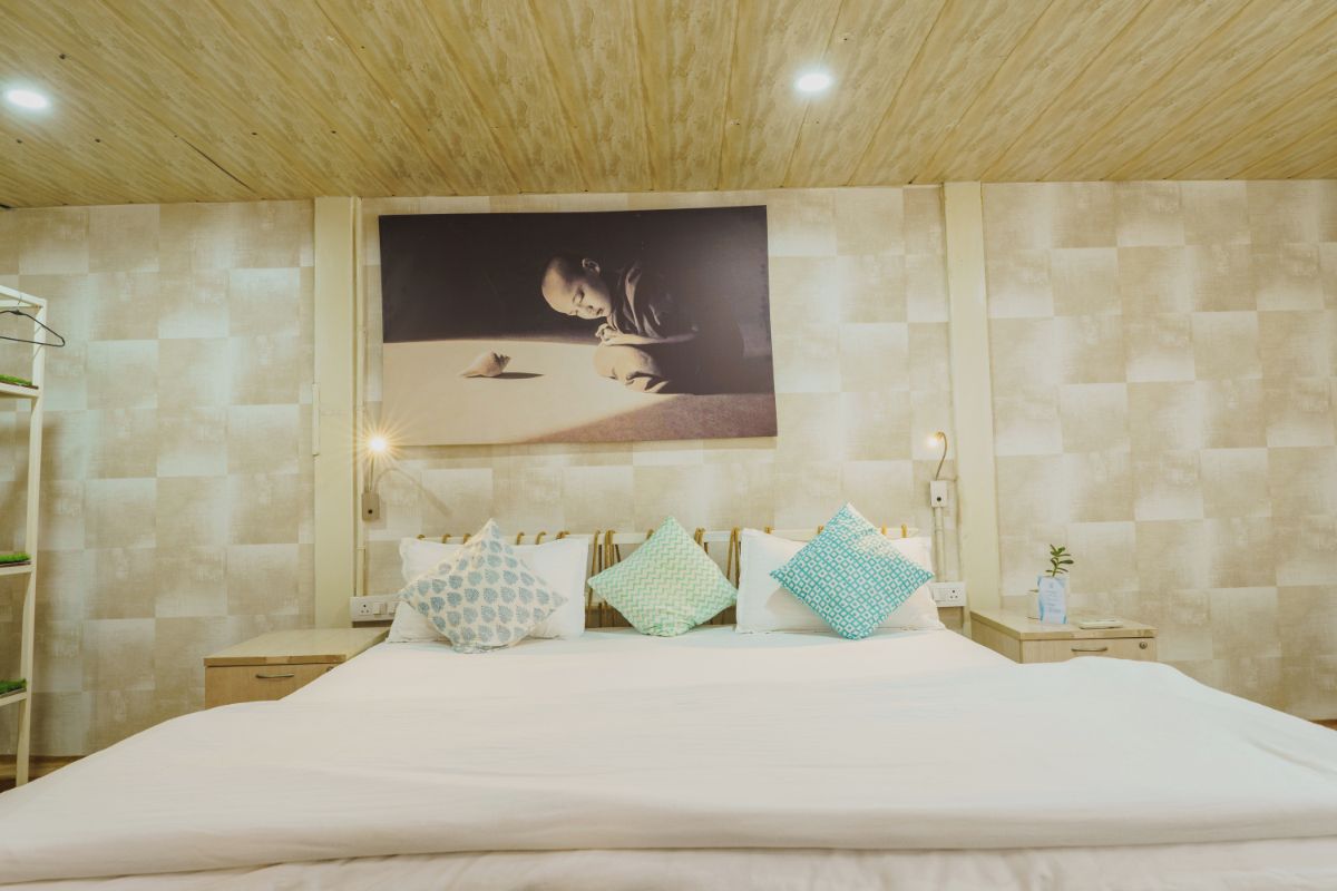 A bedroom with a bed, a nightstand, a wall-mounted picture, and a wooden ceiling.
