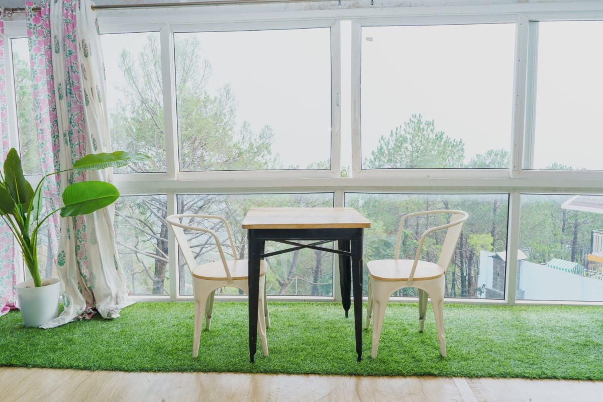 Una habitación con un ventanal grande, una mesa de madera, dos sillas y una planta en maceta.