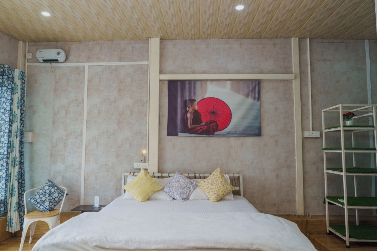 Un dormitorio con una cama, almohadas, una silla, un estante y un aire acondicionado de pared.