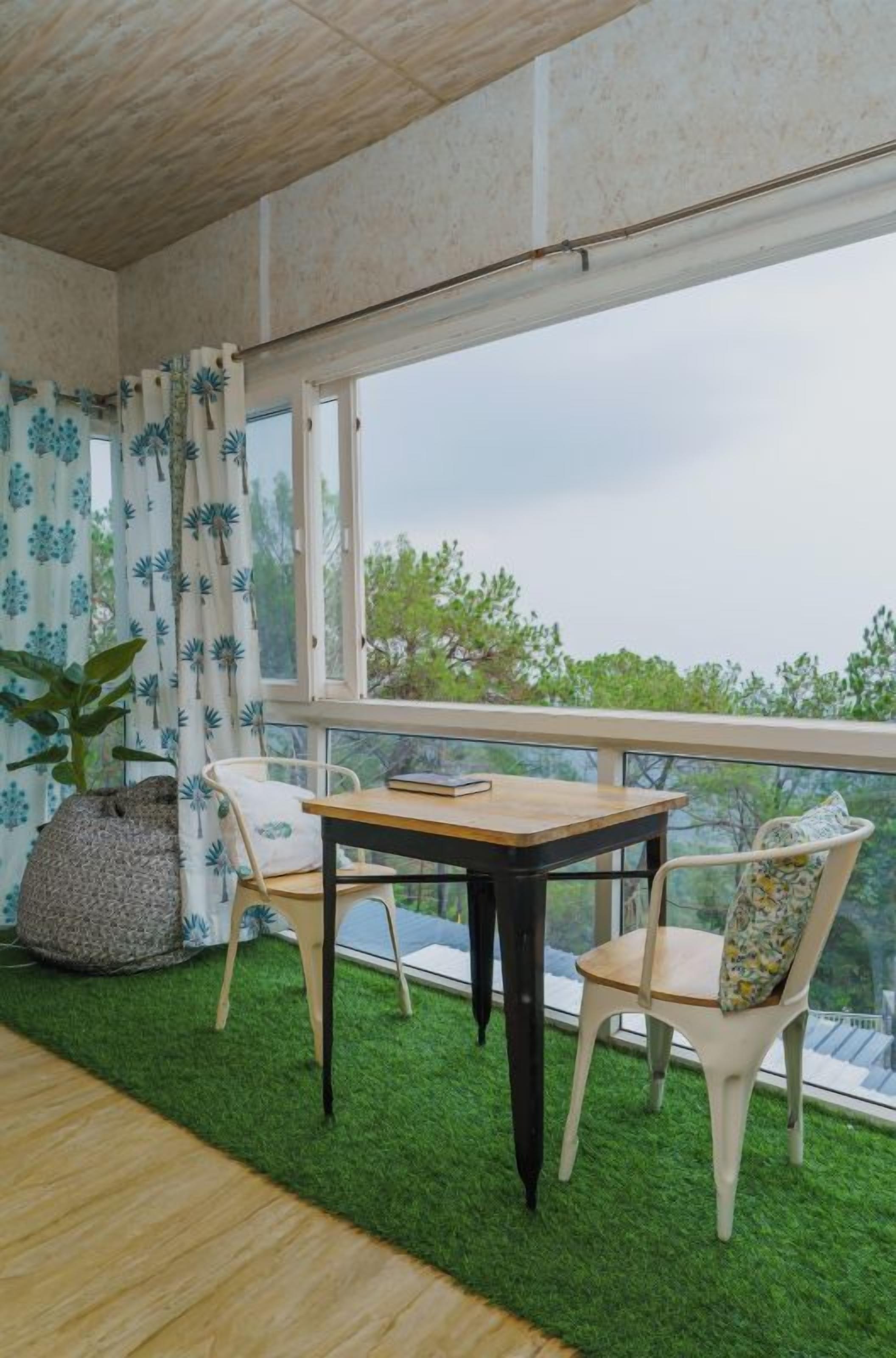 A balcony with a table and chairs, a potted plant, and a view of trees.