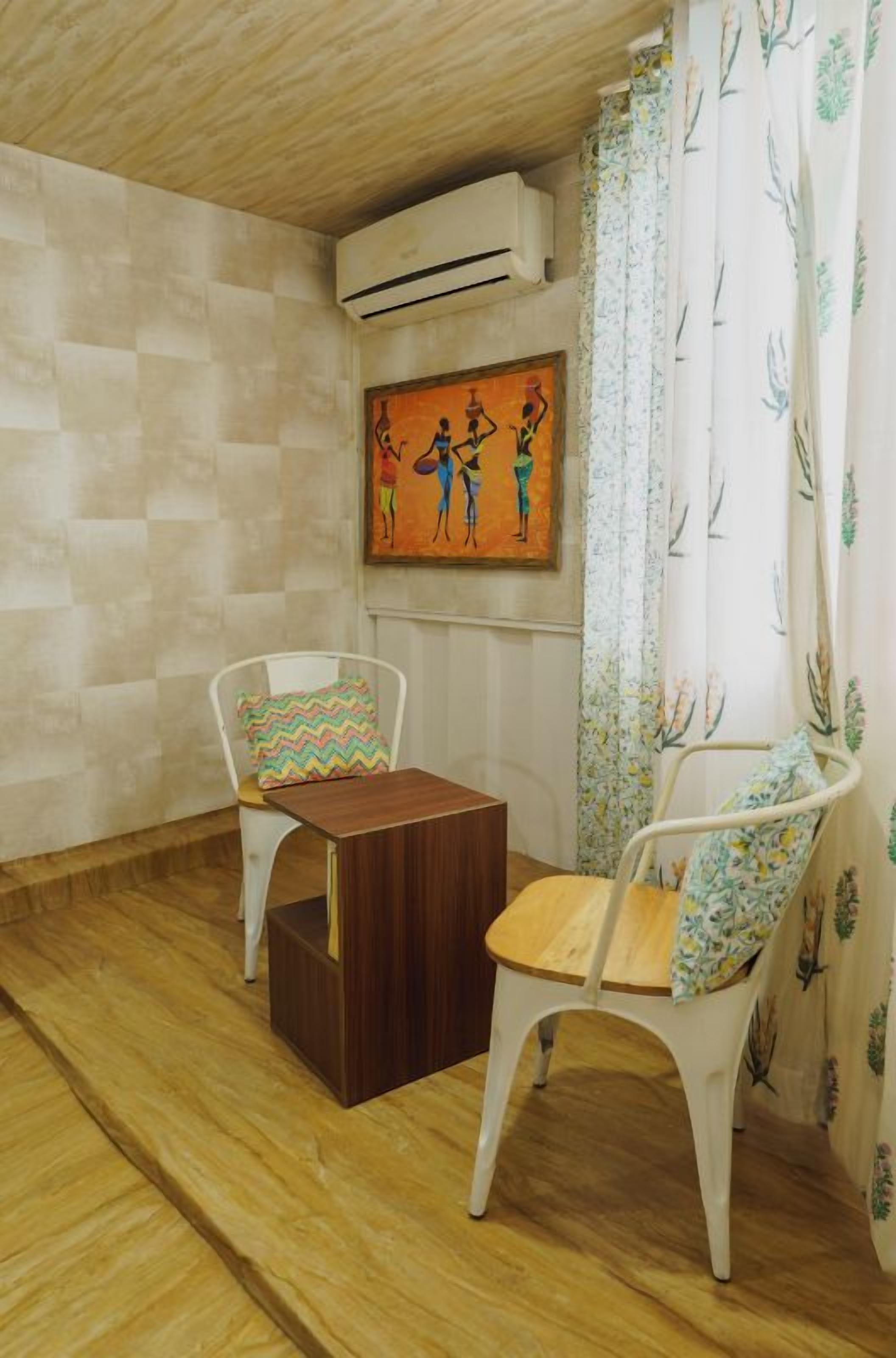 Ein Zimmer mit zwei weißen Stühlen, einem kleinen Holztisch, einem Bild an der Wand und einem Fenster mit Vorhängen.
