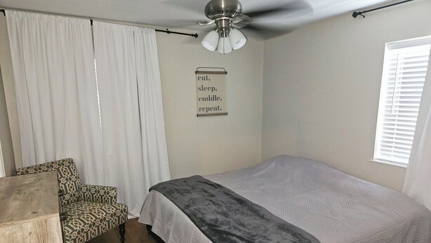 Un dormitorio con cama, una silla, un ventilador de techo y una ventana con persianas.
