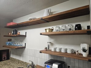 A kitchen with wooden shelves holding various kitchenware, a coffee maker, and a small plant. - Peaceful 4-bdrm HomeAway Texas Rose Euless with covered patio and fenced yard. (Euless)