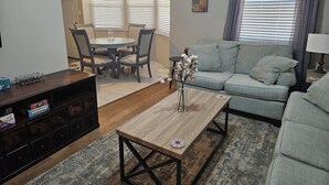 Una sala de estar con sofá, una mesa de centro, una mesa de comedor con sillas y un mueble para televisión.