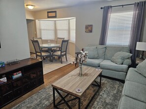 A living room with a sofa, a coffee table, a dining table with chairs, and a TV stand. - Peaceful 4-bdrm HomeAway Texas Rose Euless with covered patio and fenced yard. (Euless)