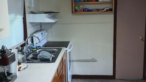 Une cuisine équipée d’une cuisinière, d’un évier et d’une étagère contenant des produits de nettoyage.
