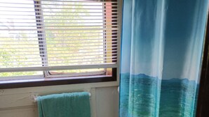 Une salle de bain avec des toilettes, une serviette accrochée au mur et une fenêtre avec des stores.