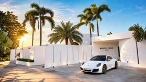 Un Porsche blanc estacionat davant d'una paret blanca on hi ha escrit 'WHITE CURE'.