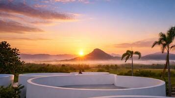 Un espacio de estar al aire libre, circular, con vista a una puesta de sol sobre un paisaje montañoso.