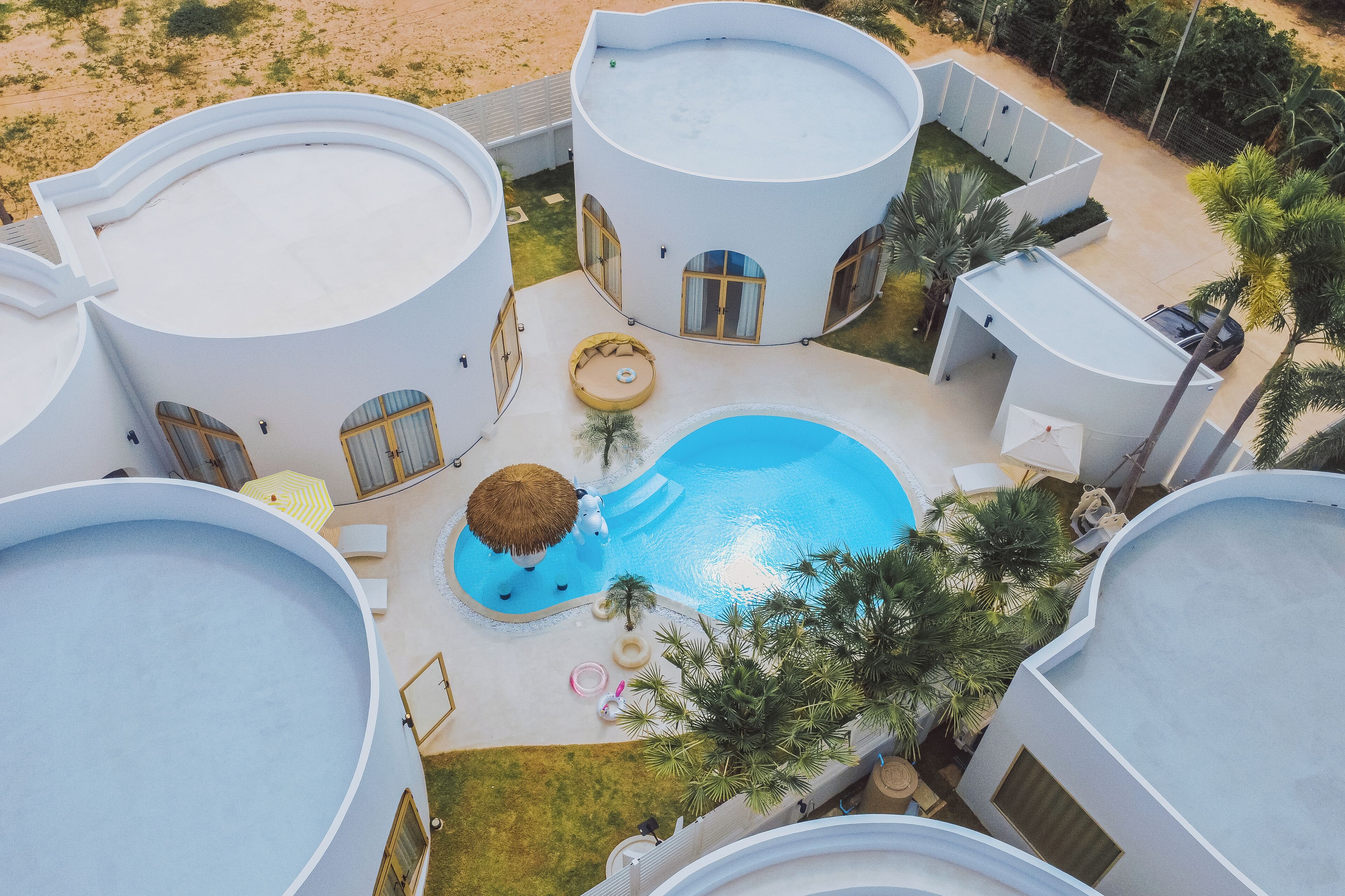 Um resort moderno com edifícios circulares interligados, uma piscina central e áreas de estar ao ar livre.