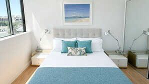 Una camera da letto con un letto, due comodini, un tavolino e una finestra, con un quadro appeso al muro.