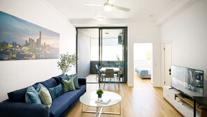 Un soggiorno moderno con un divano, un tavolino, una televisione e un quadro che raffigura un panorama urbano.