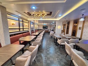 A restaurant with long tables and booths, recessed ceiling lighting, and a patterned floor. - Kaaizen Inn (Varanasi)