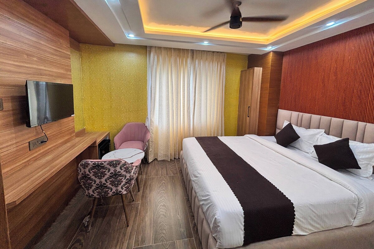 A hotel room with a bed, a desk, a chair, a television, and a ceiling fan.