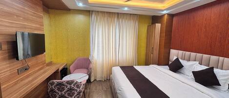 A hotel room with a bed, a desk, a chair, a television, and a ceiling fan.