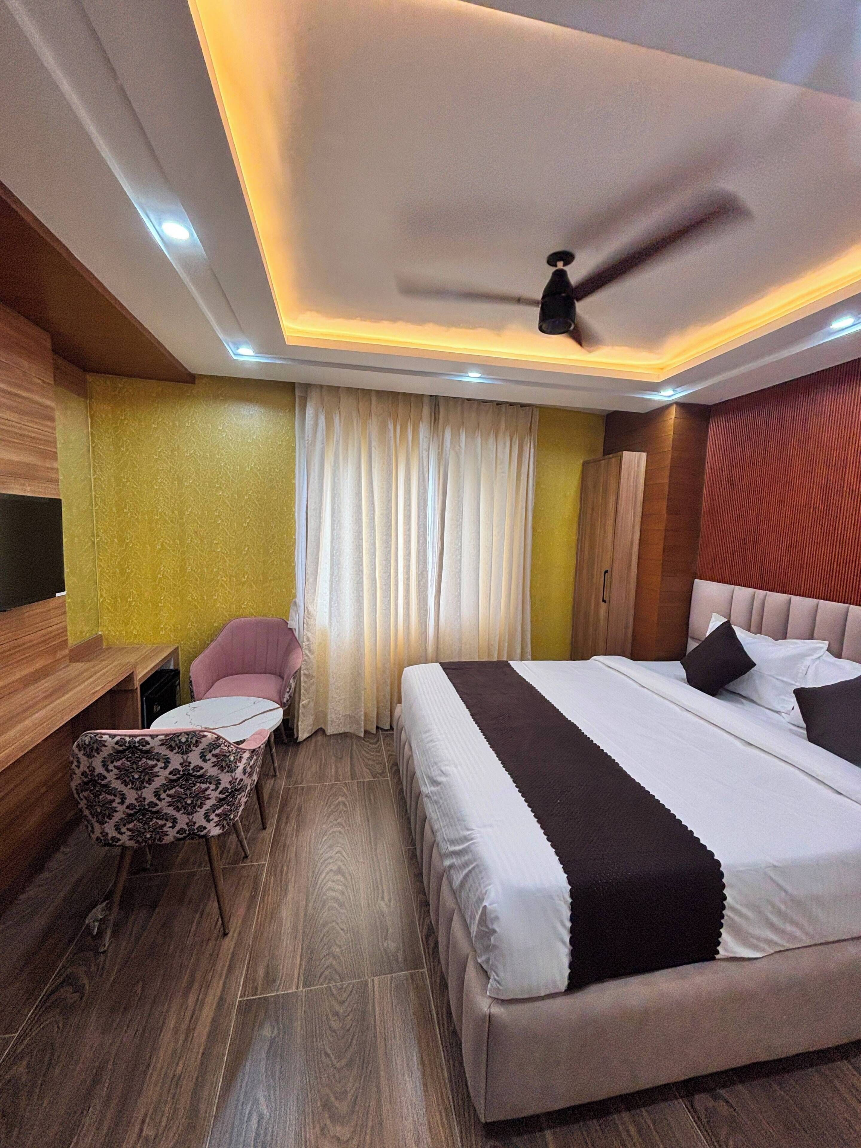 A hotel room with a bed, a desk, a chair, a ceiling fan, and a window with curtains.