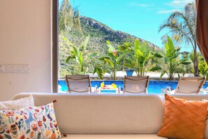 A room with a sofa, a view of a pool with chairs, and potted plants. - Villa Fonte, outstanding view, large pool (İslamlar)