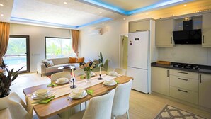 A modern kitchen with a built-in oven, a refrigerator, and a dining area with a table set for four. - Villa Fonte, outstanding view, large pool (İslamlar)