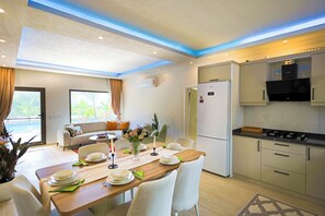 A modern kitchen with a built-in oven, a refrigerator, and a dining area with a table set for four. - Villa Fonte, outstanding view, large pool (İslamlar)