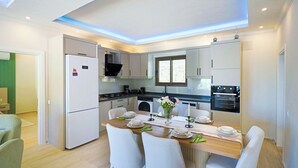 A modern kitchen with white cabinets, a dining table set for four, and a built-in oven. - Villa Fonte, outstanding view, large pool (İslamlar)