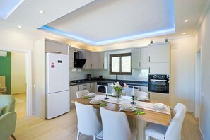 A modern kitchen with white cabinets, a dining table set for four, and a built-in oven. - Villa Fonte, outstanding view, large pool (İslamlar)