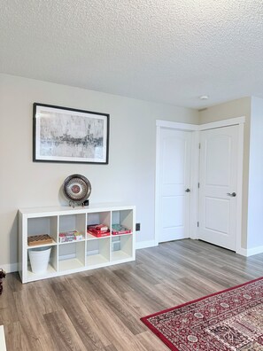 Une pièce avec une console blanche, un tableau abstrait encadré, une porte et un tapis à motifs.