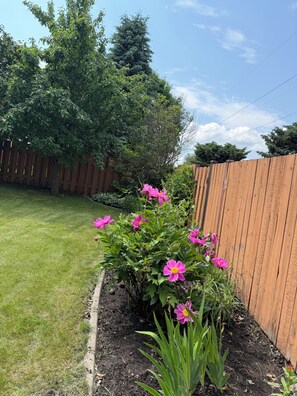 Un jardin avec des fleurs roses, une clôture en bois et une pelouse verdoyante.